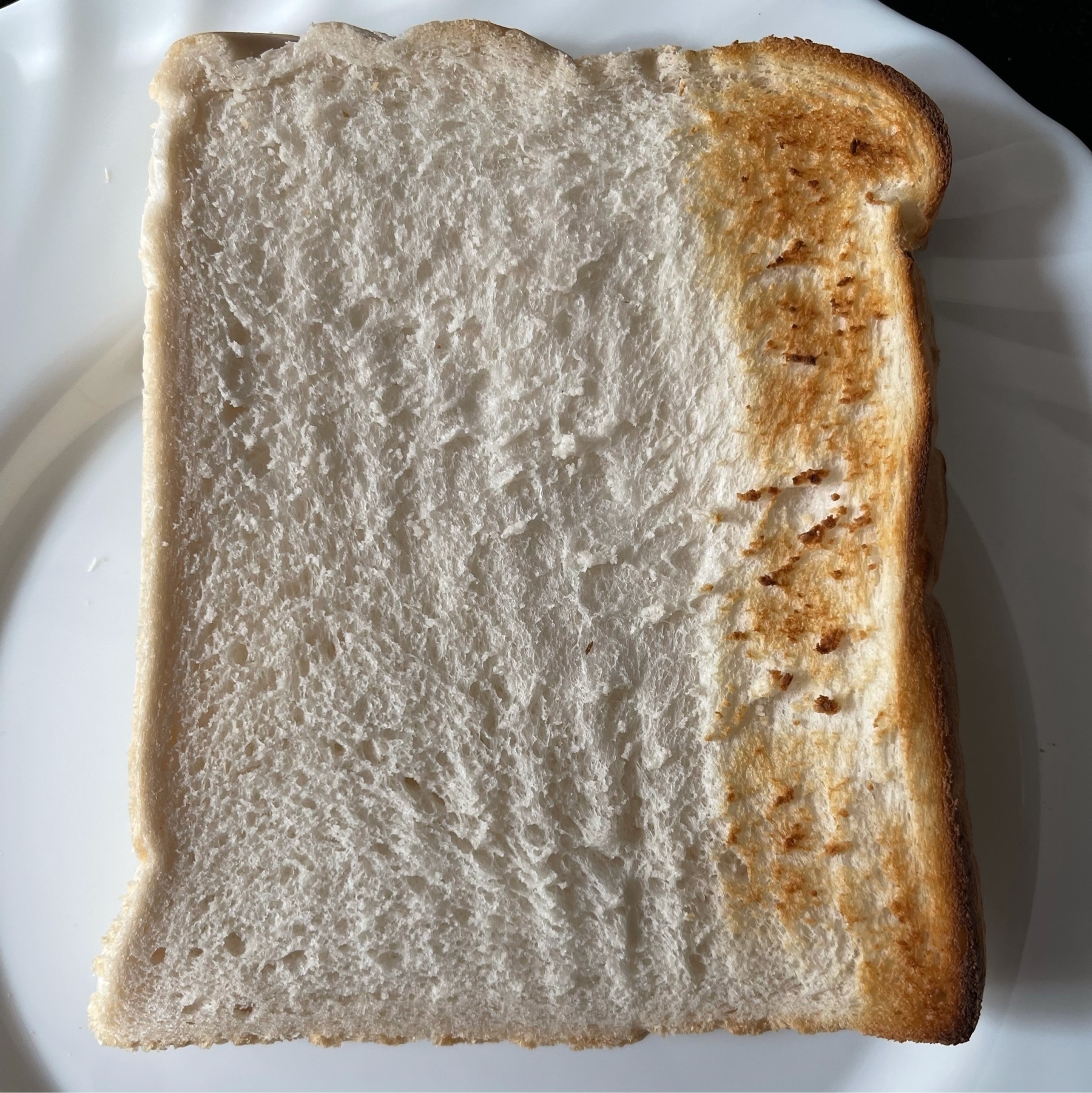 Photo of a slice of bread, with a small part toasted on one side. 