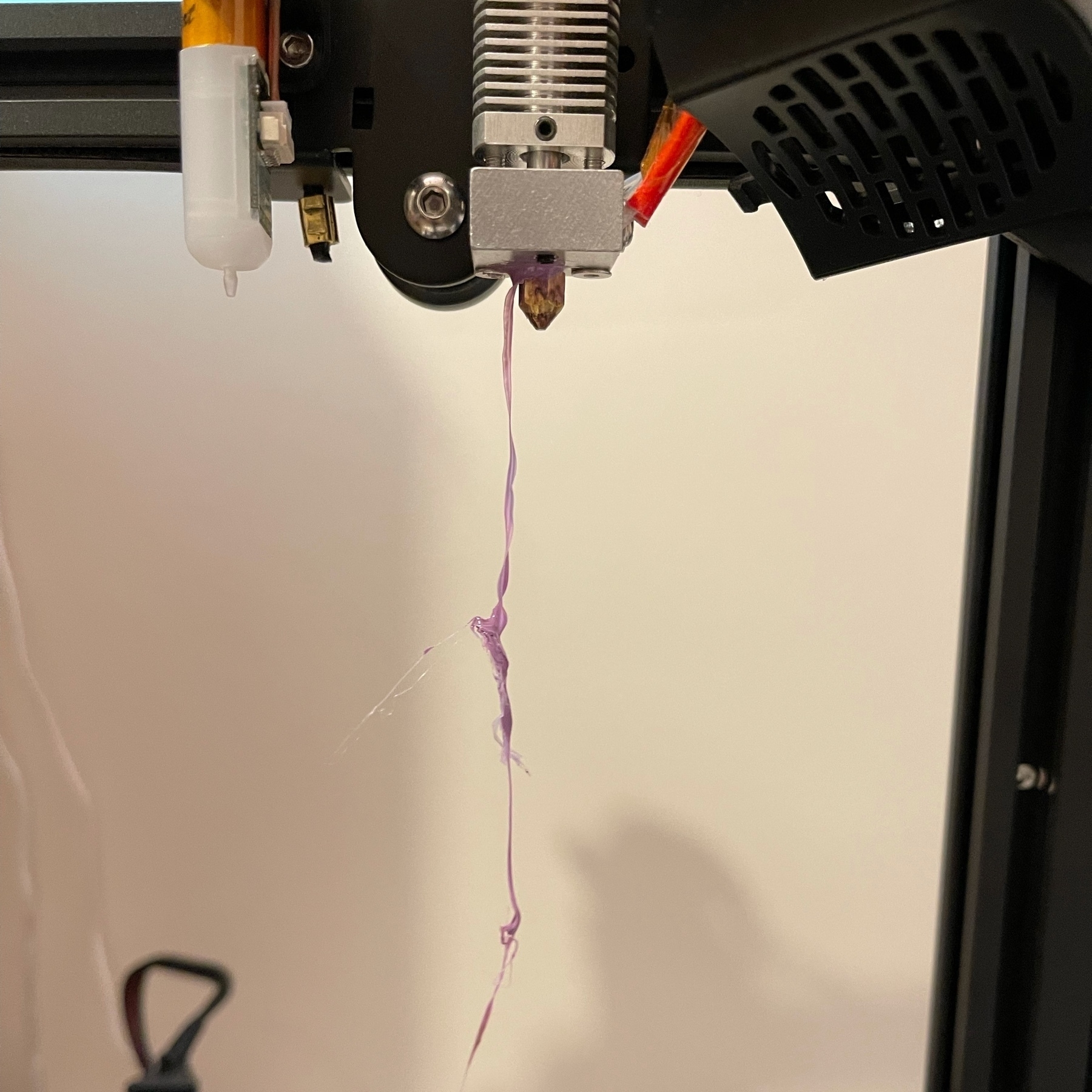 Lilac filament dangling from a bare hot end of a 3d printer. 