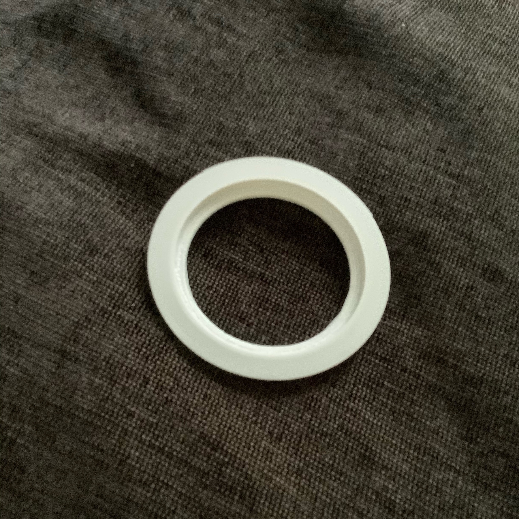 A white plastic ring with an outer lip on the top and an inner ring on the bottom.  