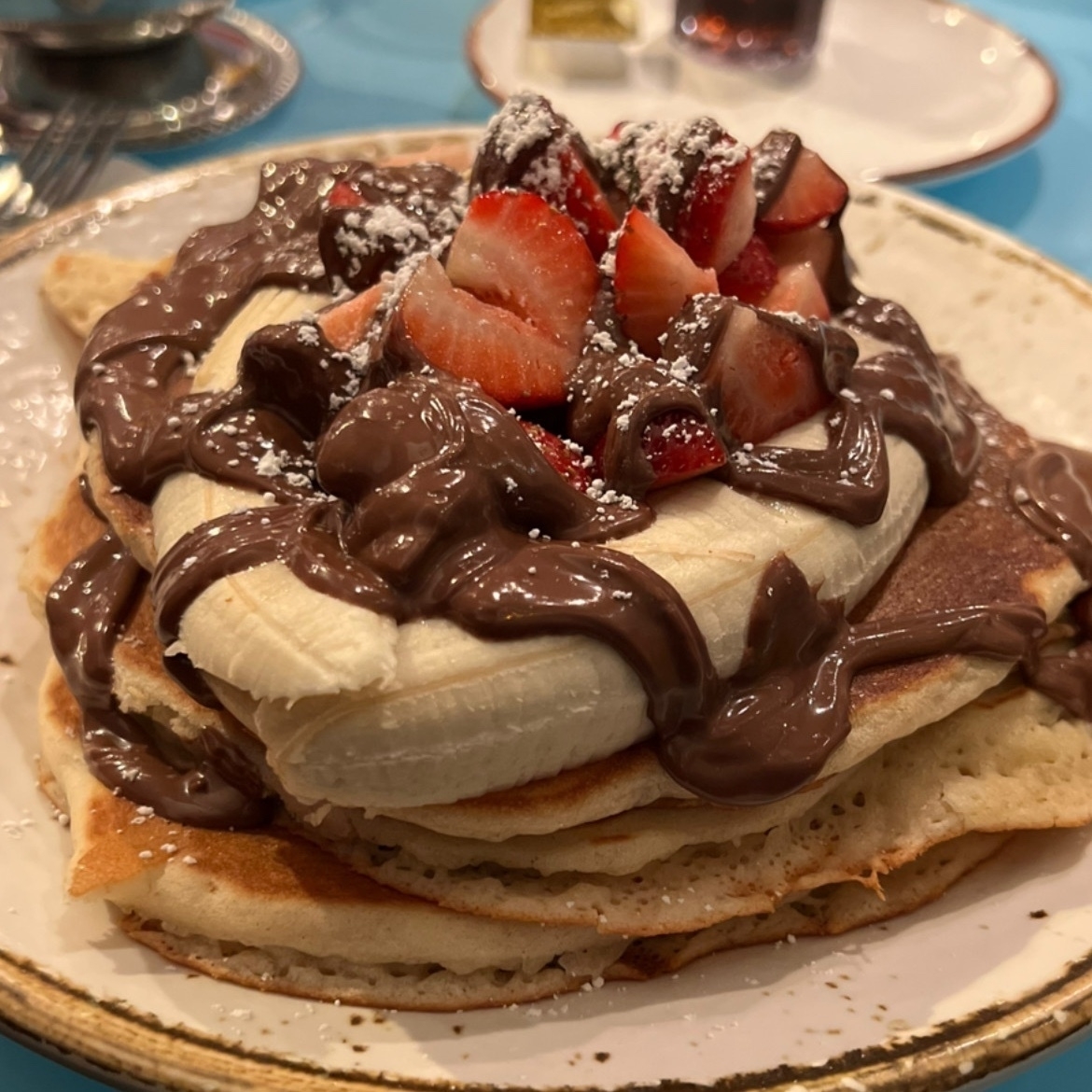 stack of 3 pancakes with banana and strawberries on top, and nutella everywhere
