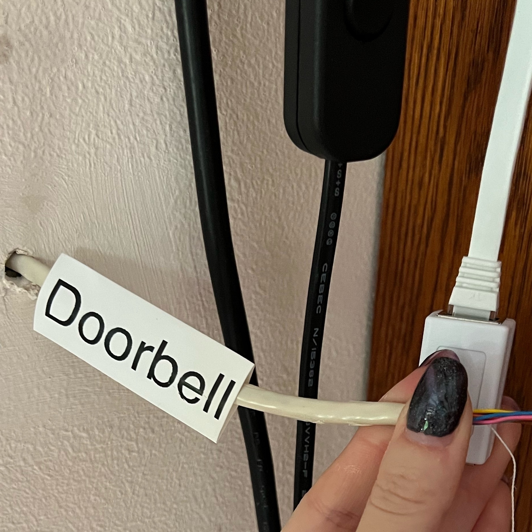 A cream wall with some grey cable casing and coloured wires coming out. A label on the cable says "Doorbell"